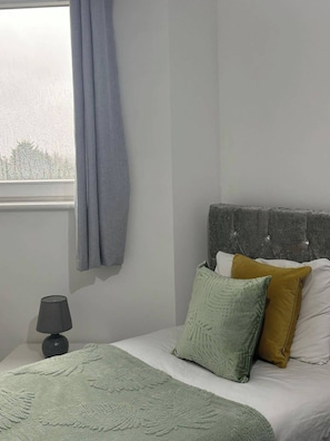 A bedroom with a bed, a nightstand, a lamp, and a window with curtains.