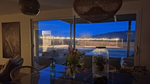 A dining area with a glass table, wicker chairs, and a view of a street with lights at dusk. - Villa with pool in the heart of Provence, Pets welcome (Montfort)