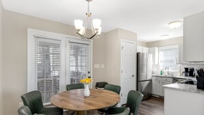 A modern kitchen with white cabinets, stainless steel appliances, and a wooden dining table with green chairs.