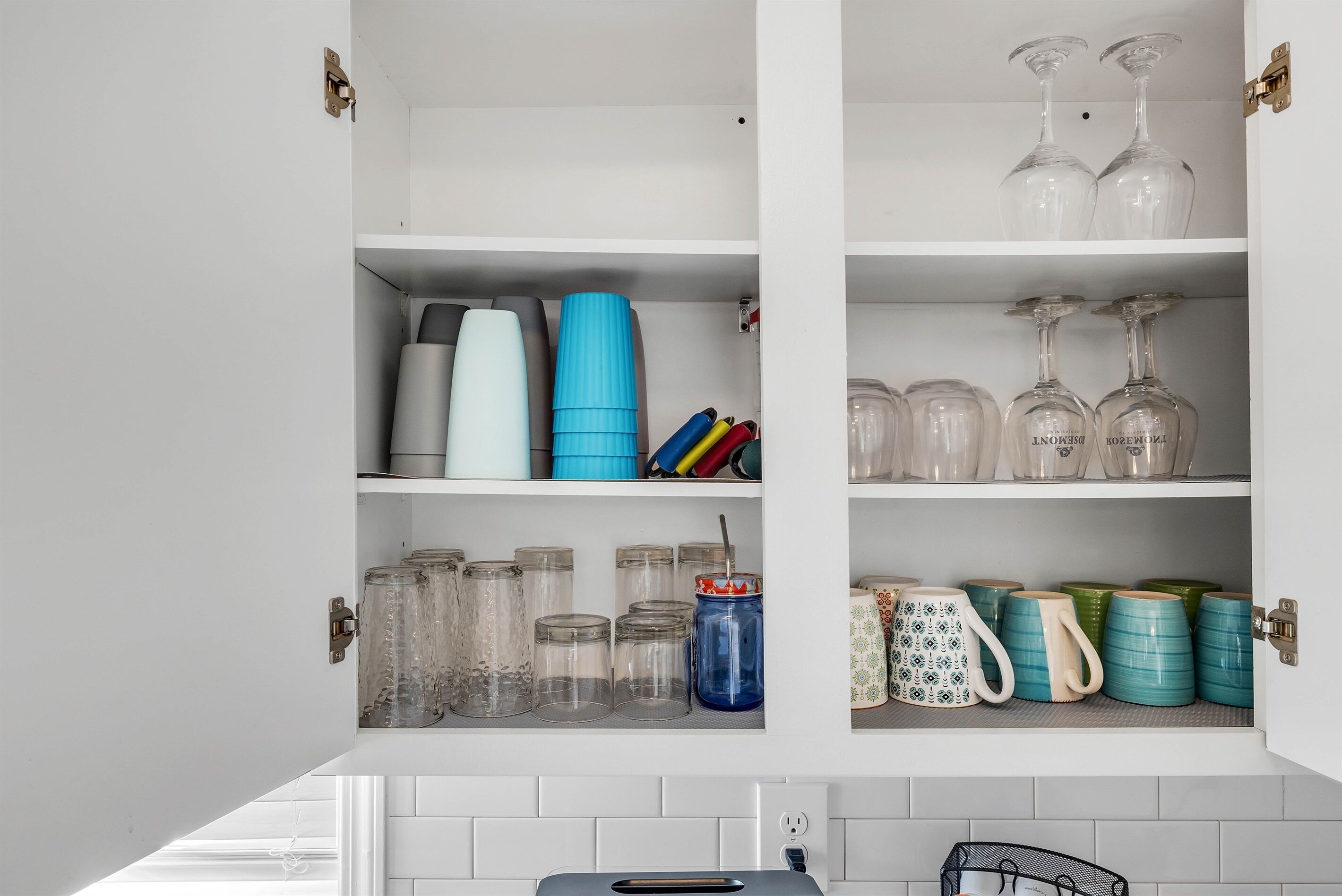 A kitchen cabinet with glass jars, mugs, and wine glasses.