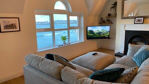 Ein Wohnzimmer mit großem Fenster zum Meer, Kamin und Fernseher an der Wand.
