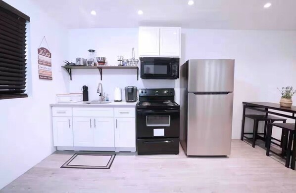 A compact kitchen with white cabinets, a black stove, a stainless steel refrigerator, and a microwave.