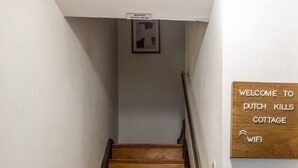 Eine Holztreppe mit einem Schild, das "WELCOME TO PUTCH KILLS COTTAGE WIFI" zeigt, und einem kleinen gerahmten Bild an der Wand darüber.