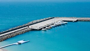 Un port esportiu amb vaixells amarrats al llarg d'un moll de formigó, envoltat d'unes aigües blaves i tranquil·les.