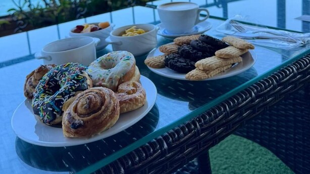 Taula amb pastissos i cafè a un balcó amb vista al mar.