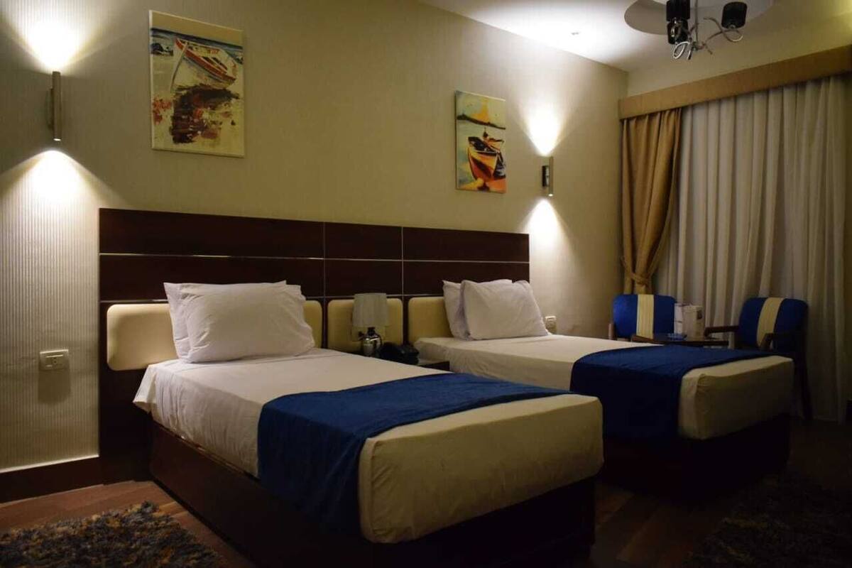 A hotel room with two single beds, a headboard, bedside lamps, and artwork on the walls.