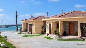 Hotel a la costa amb teulada de rajola, façana de pedra i entrada enjardinada amb escales cap a la porta.