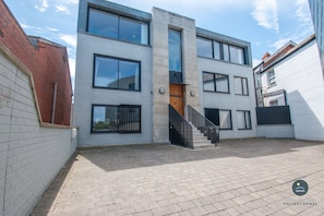 A modern two-story building with a central staircase, large windows, and a brick wall on one side.