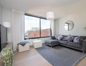 A modern living room with a grey sofa, white ottoman, and a patterned rug.