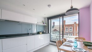 A modern kitchen with white cabinets, a black countertop, and a dining area with a table set for two. - Cockleshells - Modern apartment in Swanage (Swanage)