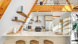 A modern kitchen with wooden beams, a central island, bar stools, and a view of the living area.