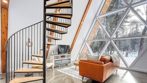 A modern interior with a spiral staircase, a large window offering a snowy view, and a cozy seating area.