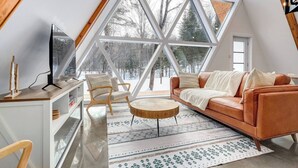A modern loft bedroom with a large skylight, a cozy seating area, and a view of a snowy landscape.