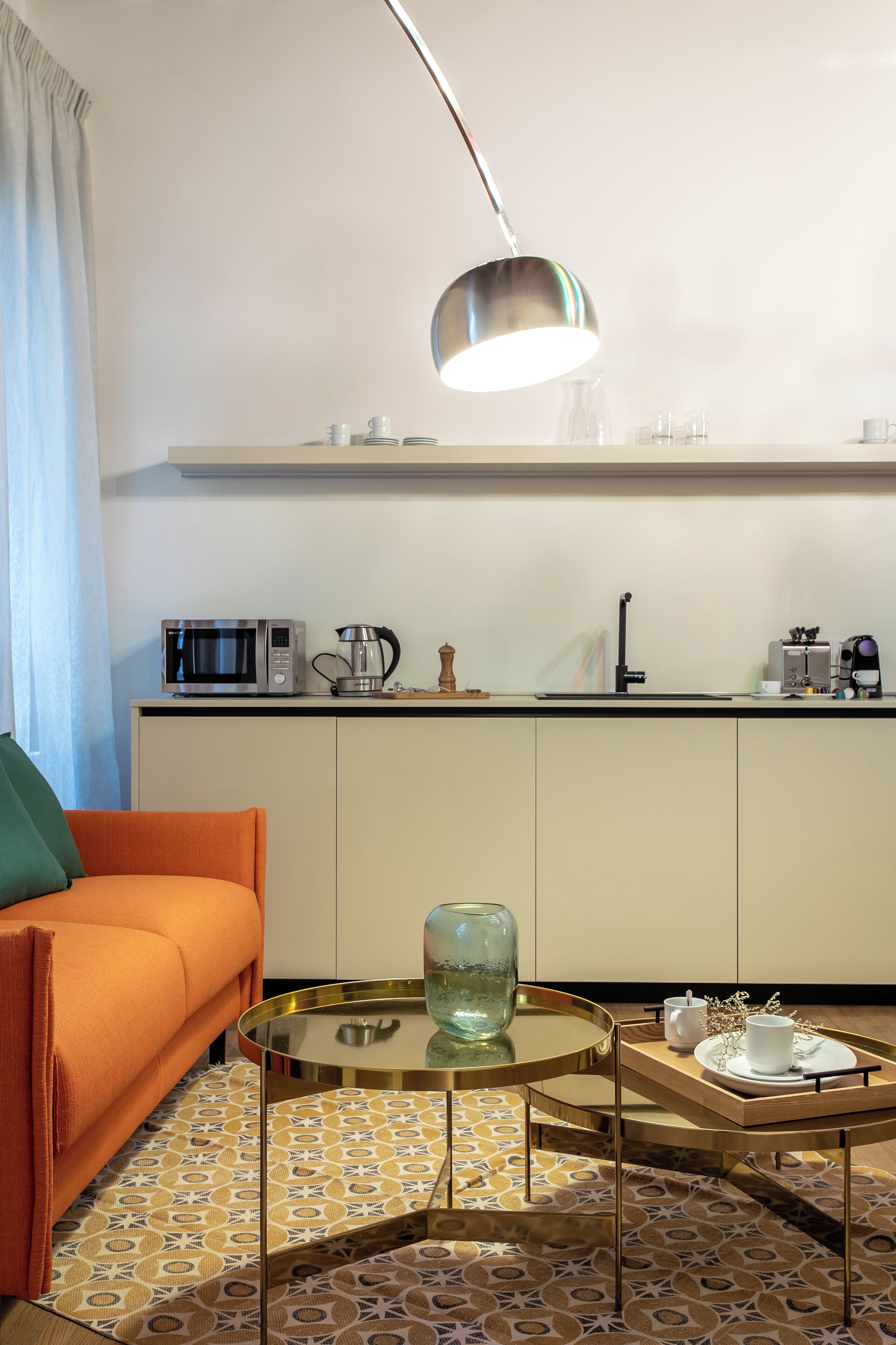 Et kompakt køkken med mikroovn, elkedel og kaffemaskine. Der er et glastopbord med bakke, en sofa og gulv med mønster.