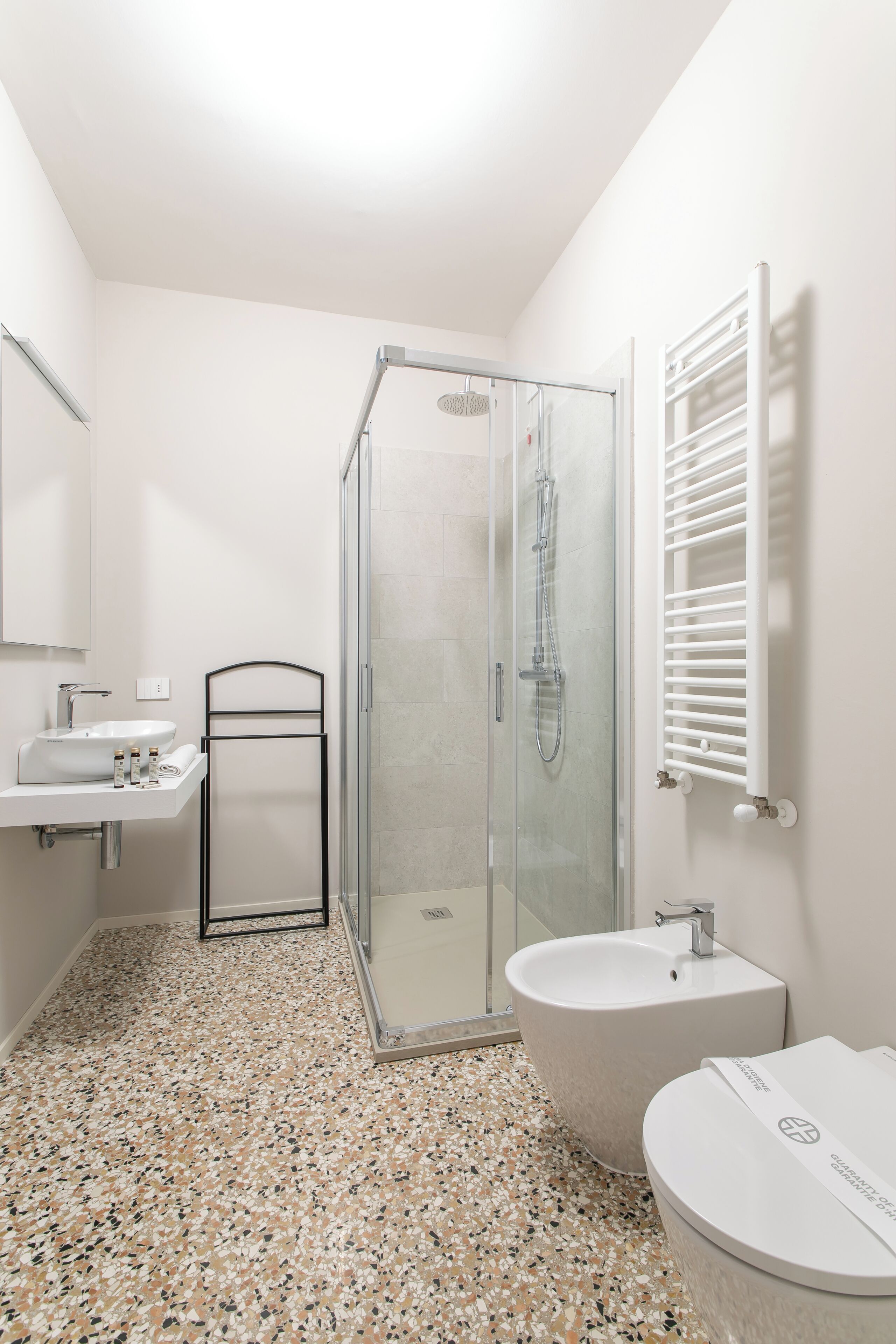 A modern bathroom with a glass shower enclosure, a freestanding sink, a bathtub, and a towel rack.