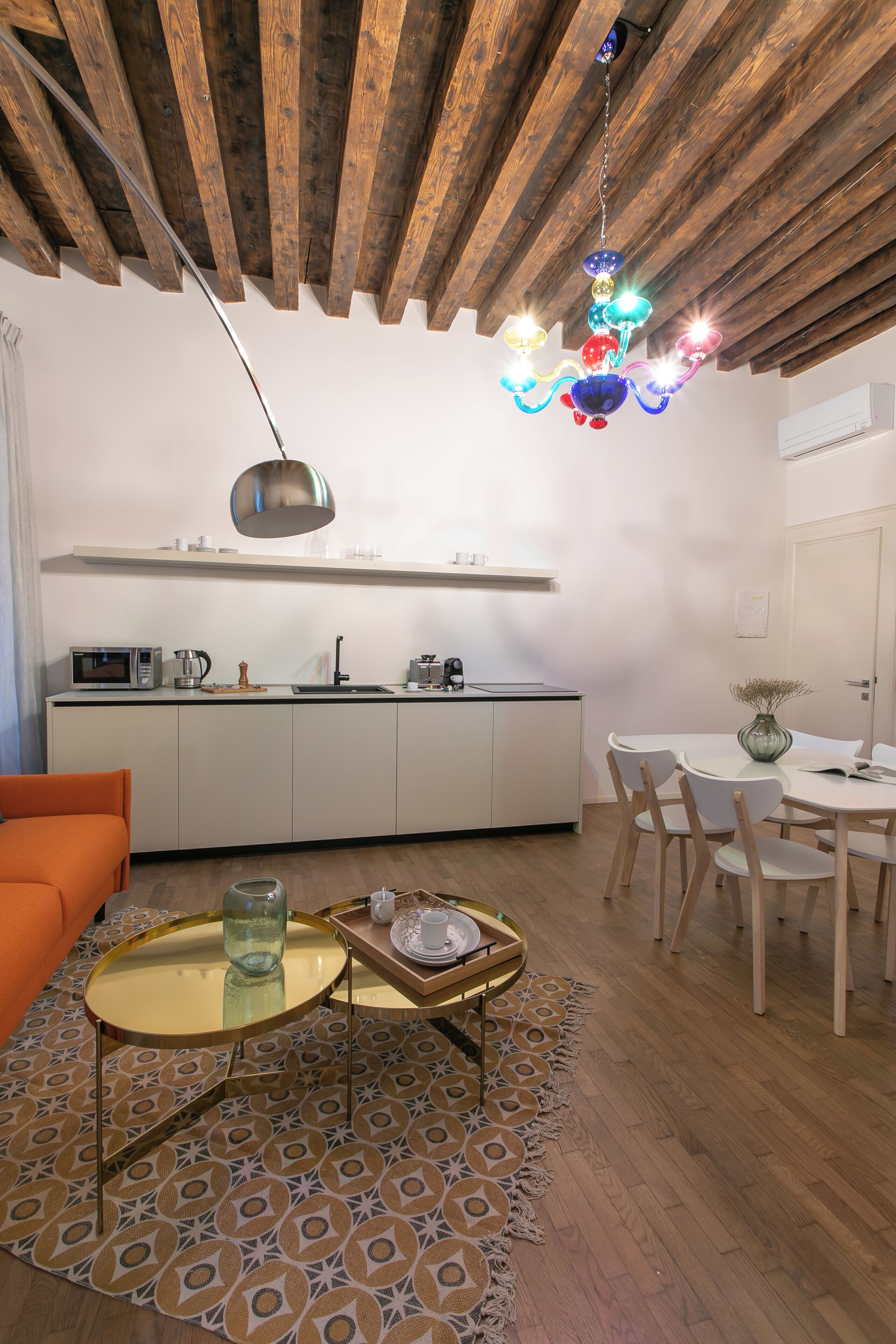 A modern kitchen with white cabinets, a microwave, and a coffee maker. There is a dining area with a round table and chairs, and a small rug with a geometric pattern.