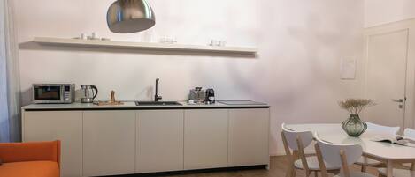 A modern kitchen with white cabinets, a microwave, and a coffee maker. There is a dining area with a round table and chairs, and a small rug with a geometric pattern.