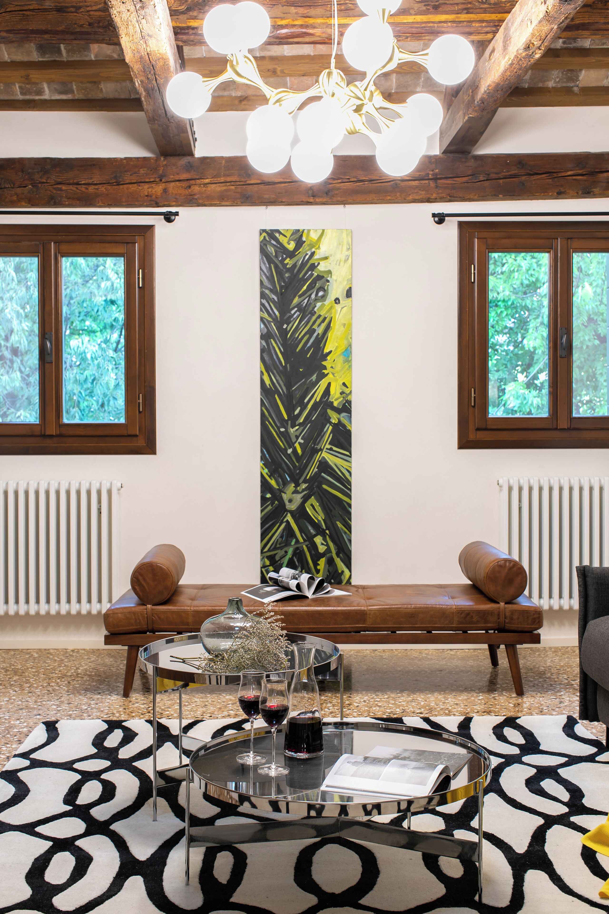 A modern living room with a wooden ceiling, a bench, a glass coffee table, and a large abstract painting.