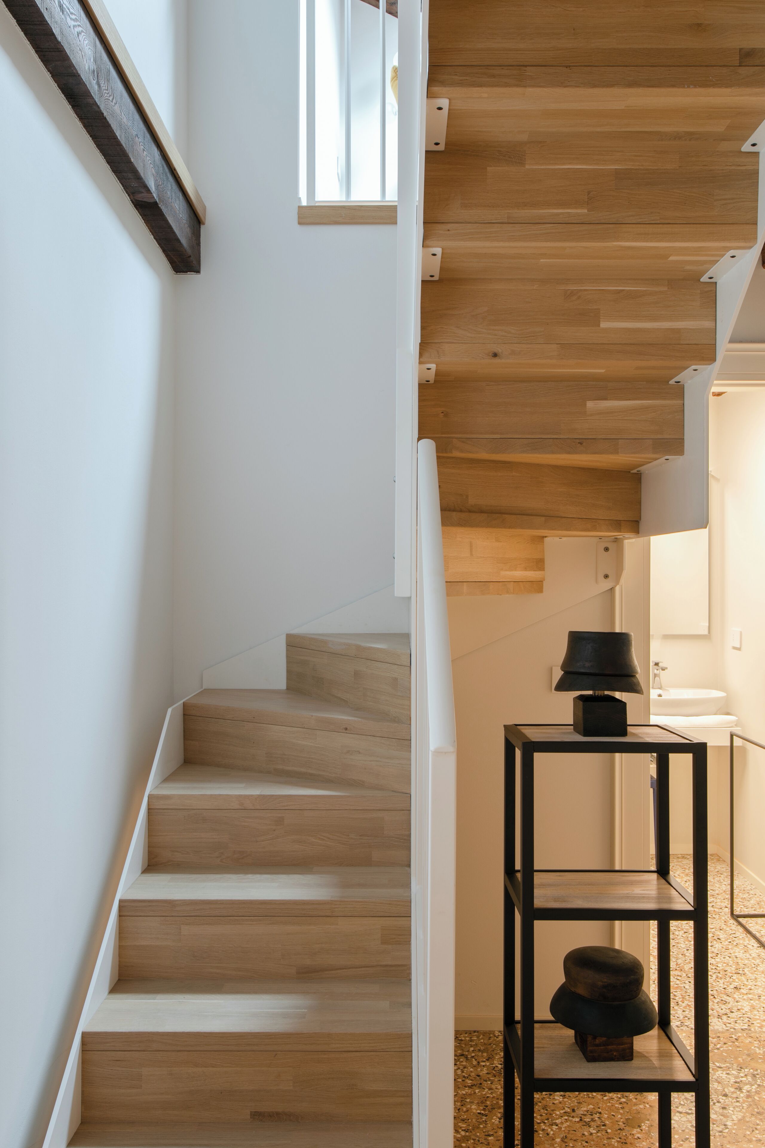 Un escalier moderne avec des marches en bois et une étagère en métal noir sur laquelle est posée une lampe.