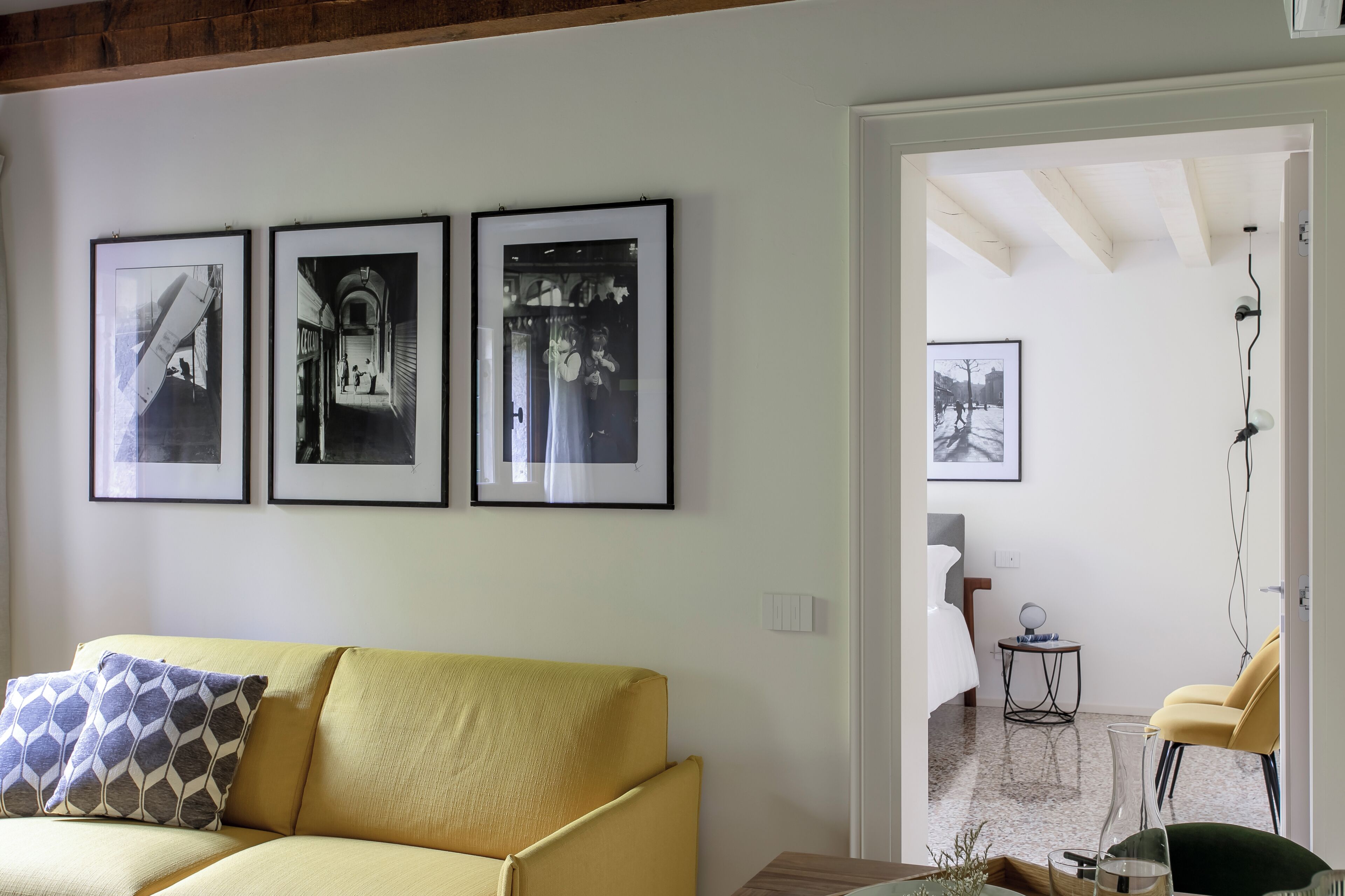 A living room with a yellow sofa, three framed photographs on the wall, and a doorway leading to another room.