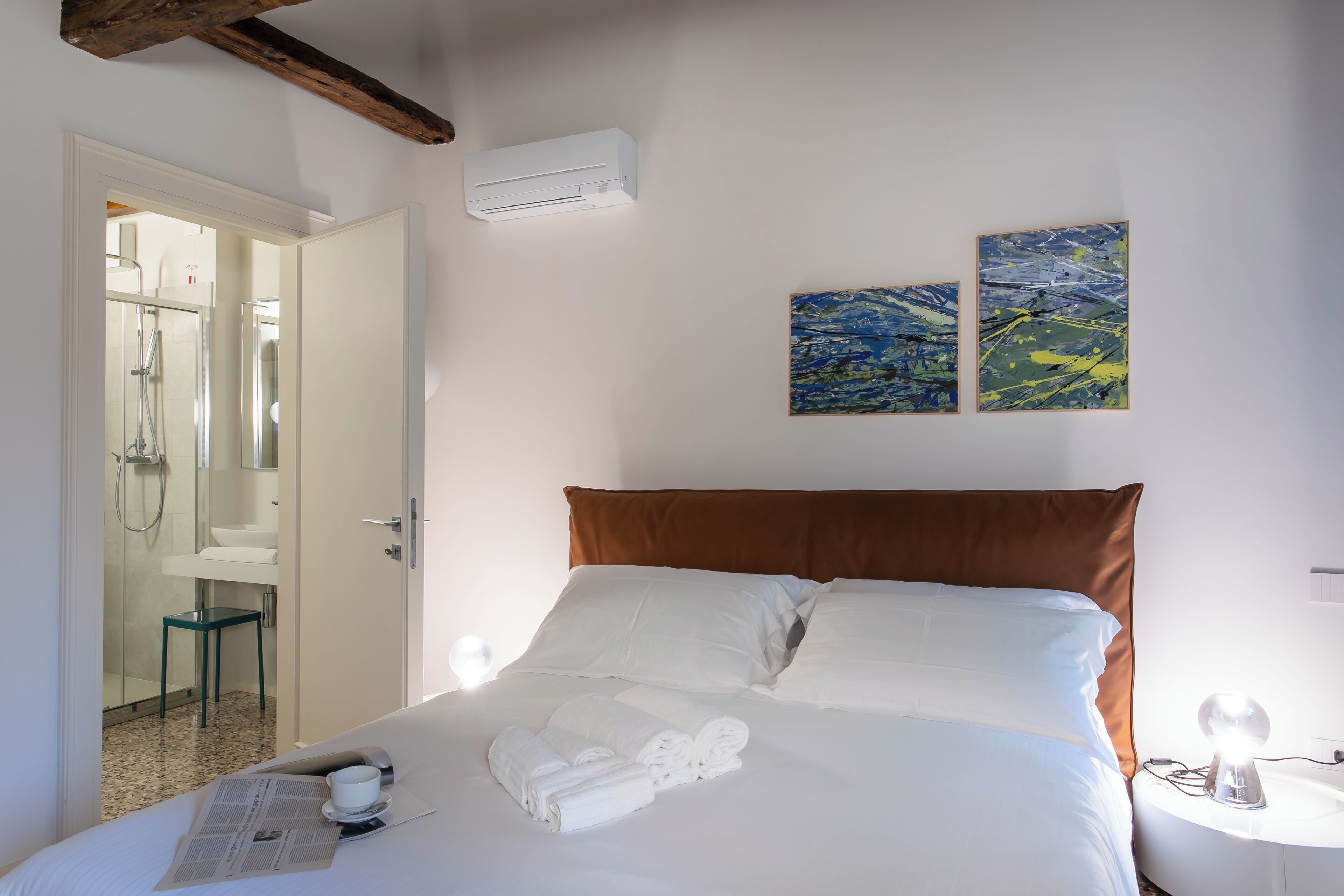 Ein Hotelzimmer mit einem Bett, einem durchgegangenen Tür sichtbaren Badezimmer und zwei abstrakten Bildern an der Wand.