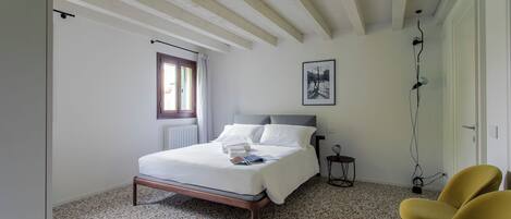 A bedroom with a bed, a window, a radiator, a framed picture, and a chair.