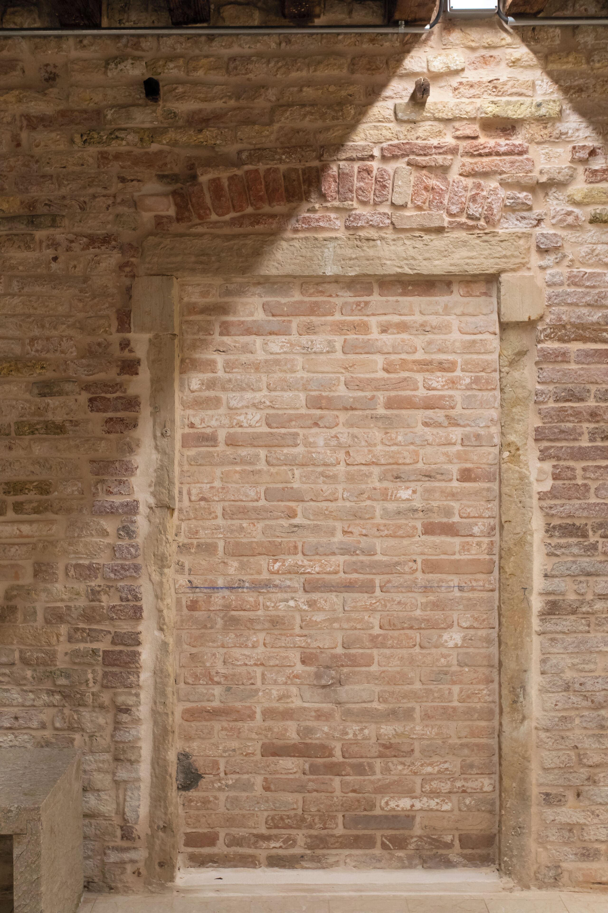A brick wall with a narrow opening, possibly a door or window, in a rustic building.