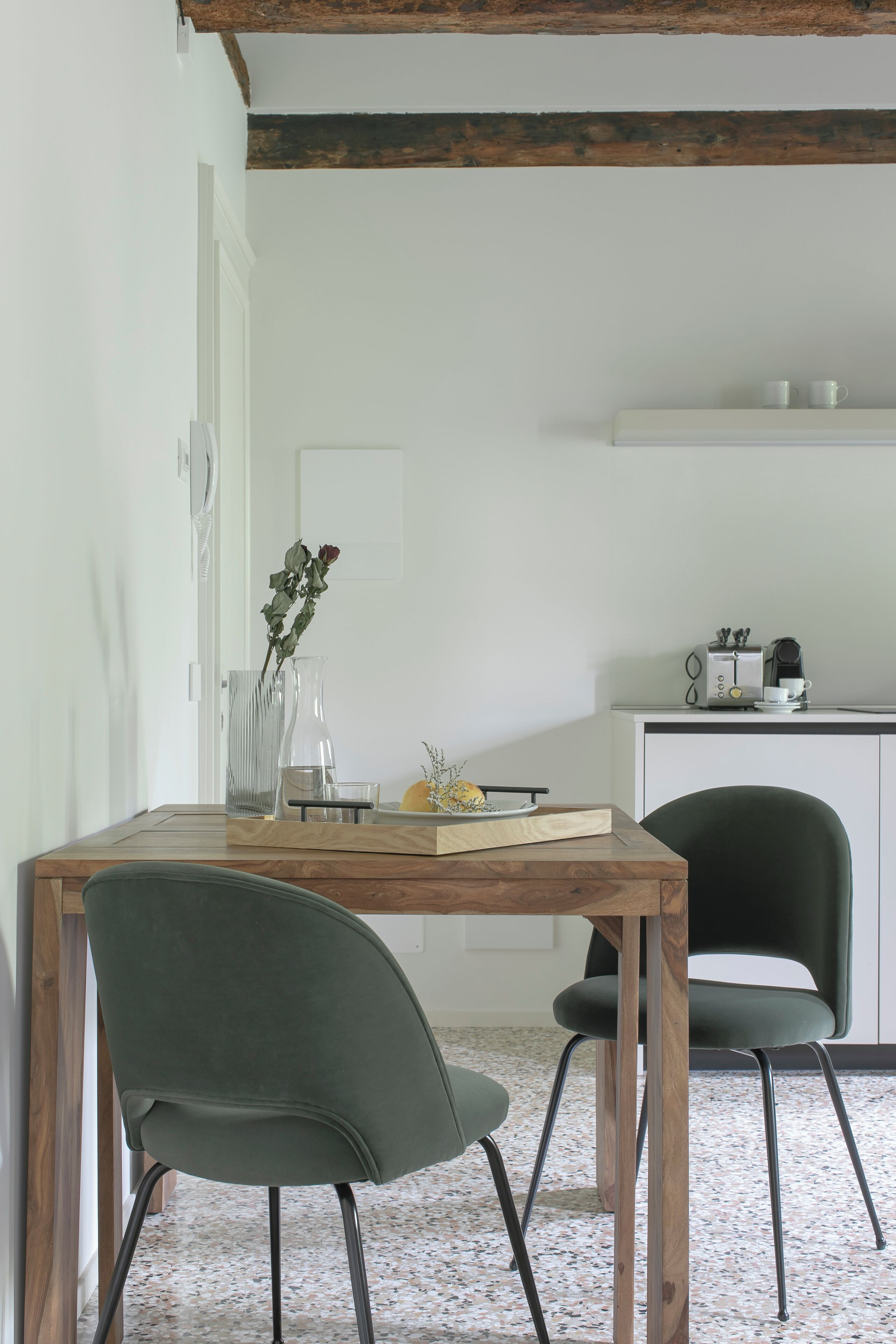 Een eethoek met een houten tafel, twee stoelen, een vaas met bloemen en een keuken op de achtergrond.