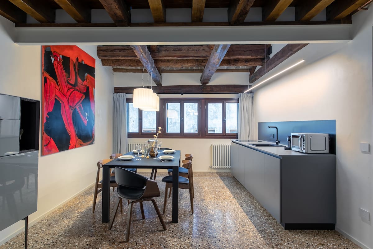 A modern kitchen with a dining area, granite flooring, and a large abstract painting on the wall.