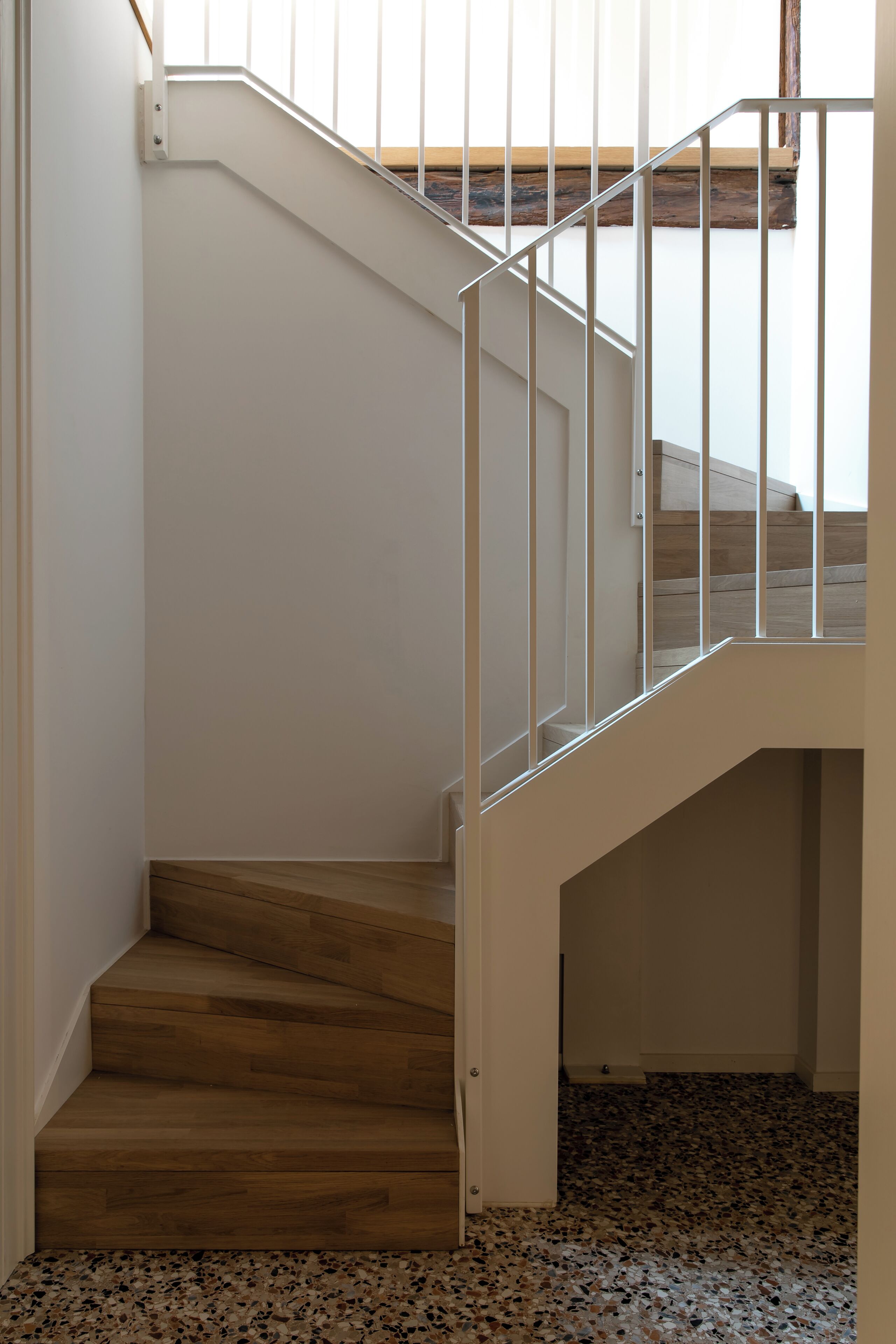 Una escalera de madera con barandillas blancas que conduce a un rellano con suelo de madera.