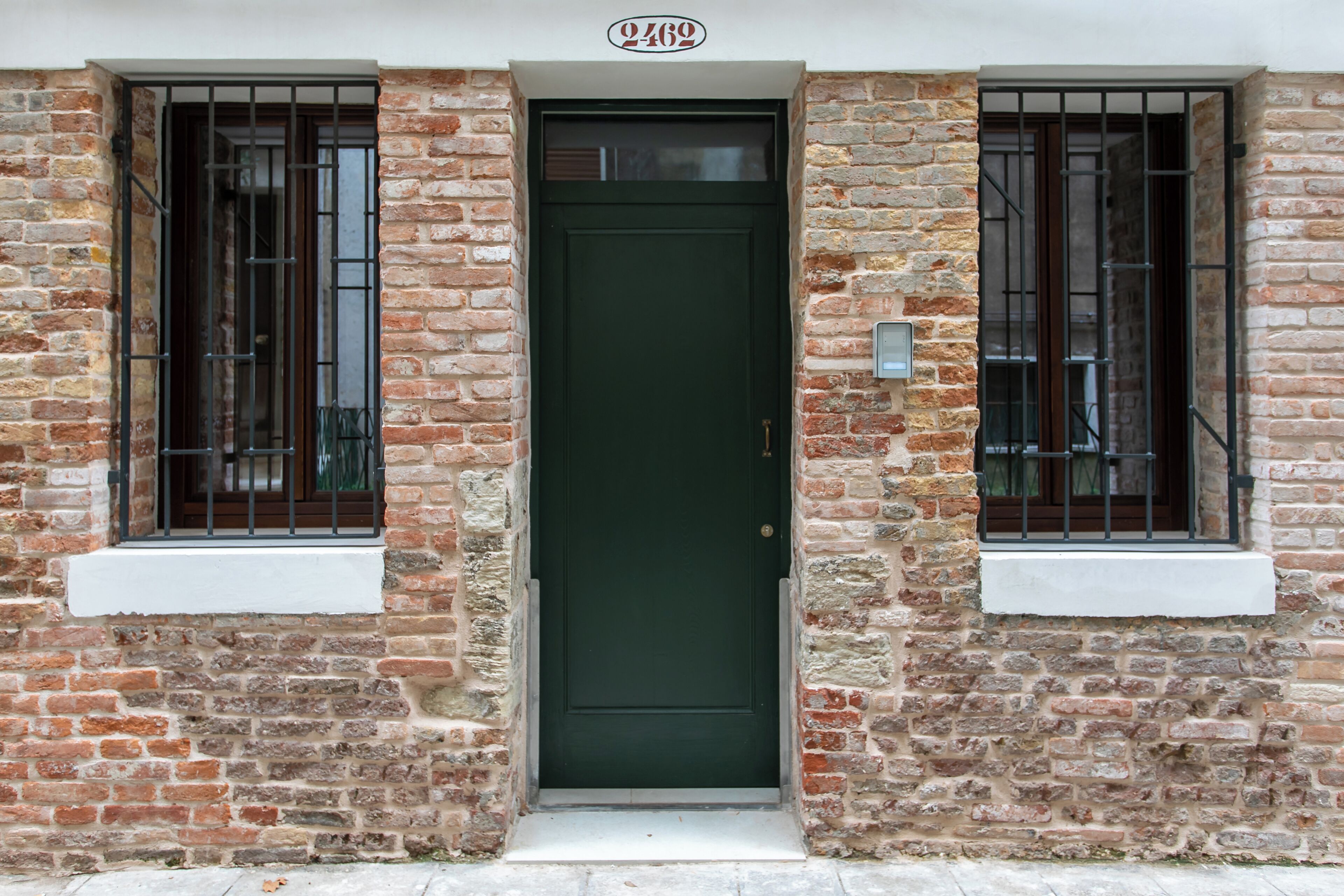Un bâtiment en briques avec une porte verte et deux fenêtres grillagées.
