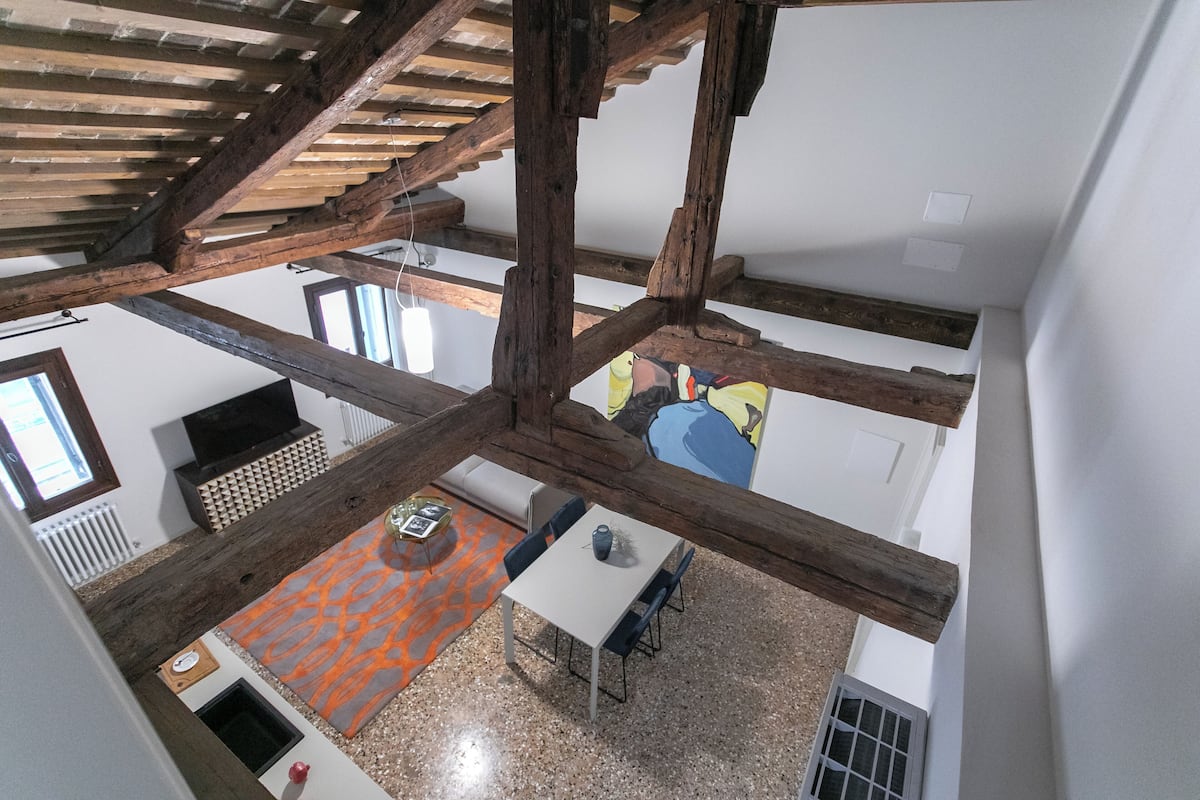 A high-ceilinged room with exposed wooden beams, a fireplace, and a dining area with a table and chairs.
