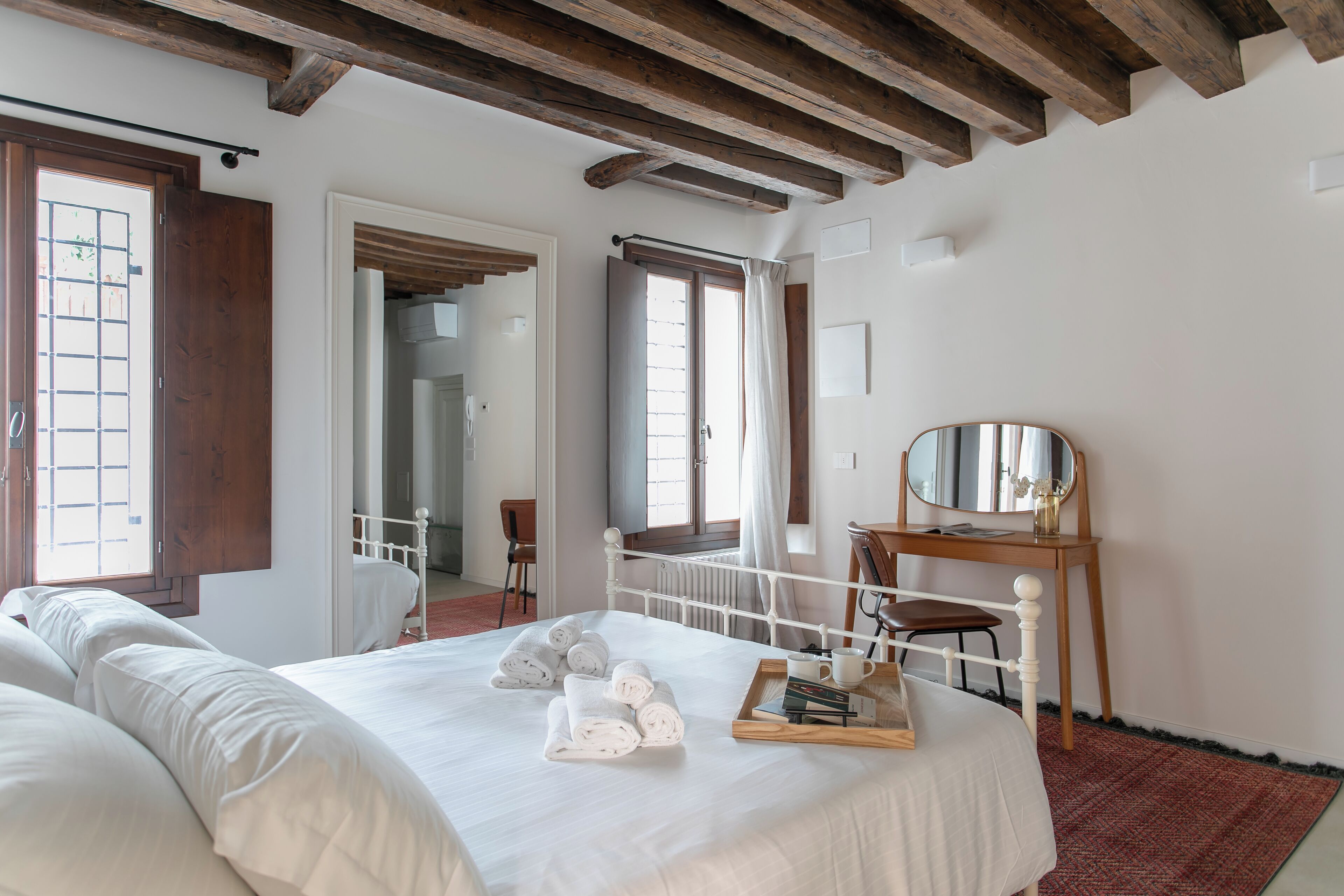 Ein Schlafzimmer mit einem großen Bett, einem Holztisch, einem Spiegel und Blick auf einen Balkon.