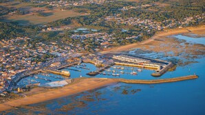 Vue aérienne d’une ville côtière avec un port de plaisance, des plages de sable et des quartiers résidentiels.