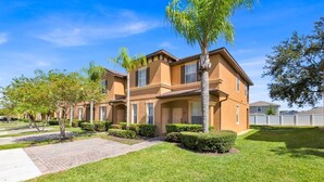 A multi-story residential building with a brick facade, multiple windows, and a well-maintained lawn with trimmed hedges.