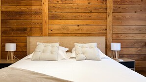Un dormitorio con cabecera de madera, dos lámparas de noche y una cama bien tendida con ropa blanca.