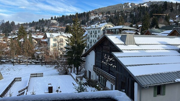 A snow-covered building with a wooden facade and a balcony, surrounded by other buildings and a snowy landscape.