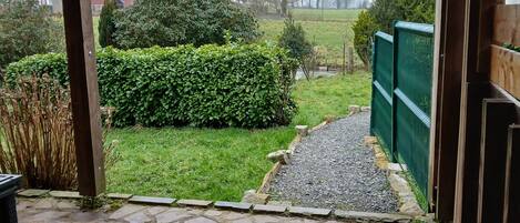 A stone-paved entrance to a covered outdoor area with a view of a green lawn and a hedge.