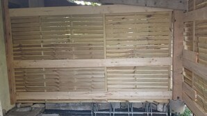 Een houten constructie met een lambrisering, een vloer van zwarte mat en een klein witte bak.