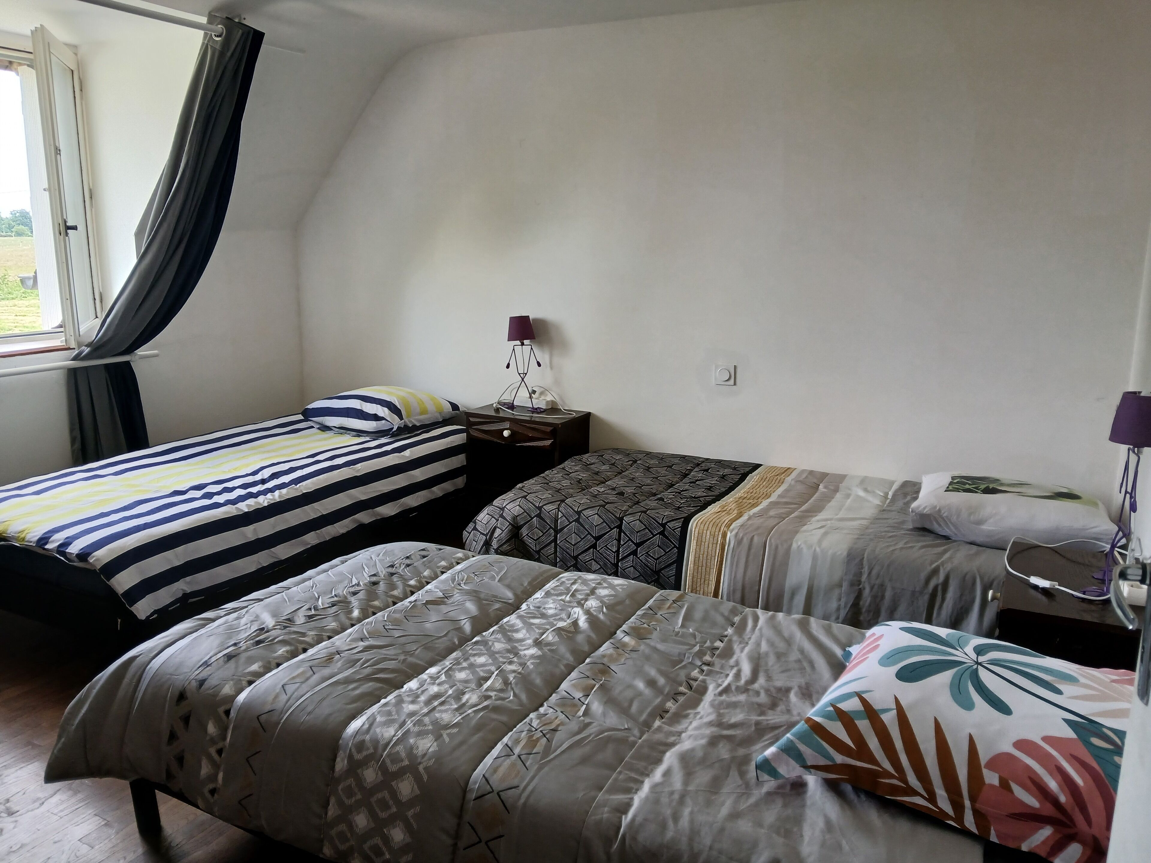 Une chambre avec deux lits, une fenêtre avec des rideaux, une table de chevet avec une lampe et une prise électrique au mur.