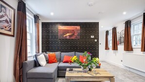Una sala de estar moderna con un sofá seccional gris, una mesa de centro de madera con un centro de mesa floral y un cuadro de un paisaje urbano en la pared.