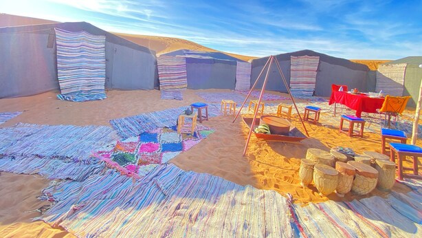 A desert camp with tents, a dining area with red tablecloth, and colorful rugs. - Merzouga Traditional Camp (Taouz)
