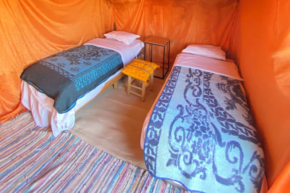 A tent-like room with two beds, a hanging light, and a small stool.