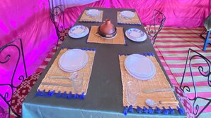 A dining table set for four with a central pot, surrounded by plates and glasses, under a tent-like structure. - Merzouga Traditional Camp (Taouz)