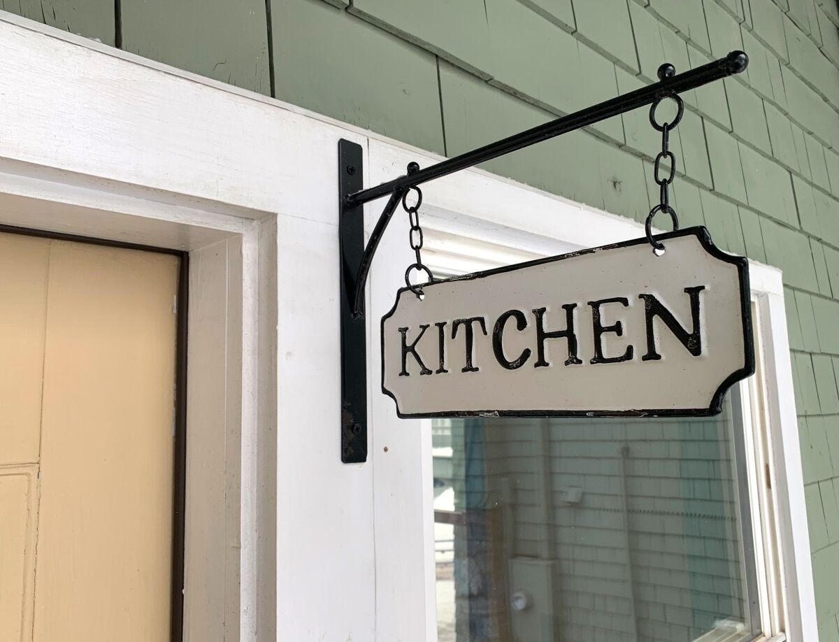 A sign hanging from a metal bracket that reads "KITCHEN".