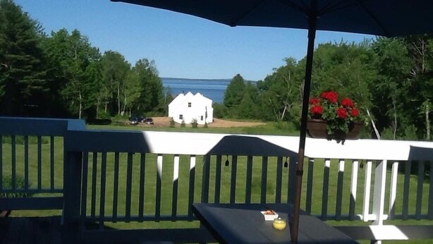 A wooden deck with a white railing, a picnic table, and a hanging planter with red flowers. - The Northport Inn & Lodge (Belfast)