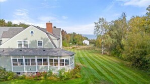 A house with a large bay window, a well-maintained lawn, and a view of the ocean. - The Northport Inn & Lodge (Belfast)