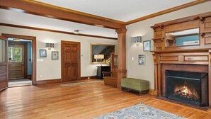 A spacious living room with hardwood flooring, a fireplace, and a large mirror. - The Northport Inn & Lodge (Belfast)