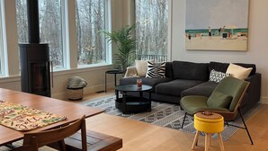 Un salon moderne avec une cheminée, de grandes fenêtres, un ventilateur de plafond et un tableau au mur.