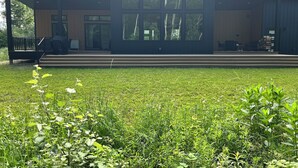 Un bâtiment moderne doté d’un espace extérieur couvert, d’un escalier menant à une terrasse et d’une pelouse à l’avant.